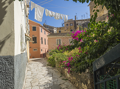 Corfu老城的Corfu 狭窄的可腐石街 有粉红色布干维尔花朵 传统的希腊人房屋 挂着干白色洗衣衣服 蓝天夏日阳光明媚图片