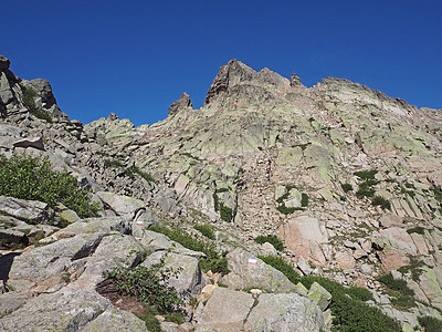 科西嘉阿尔卑斯山的高山风景 有绿色灌木和红白标示的陡峭路径 著名的 gr 20 轨道 蓝天背景图片