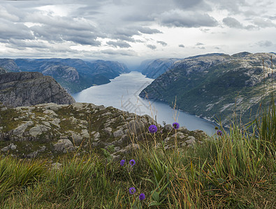 Lysefjord 峡湾的景色 紧邻巨大的悬崖著名的挪威观点 那里盛开着紫罗兰色的花朵 喜怒无常的天空 秋天的一天 自然和旅游背图片