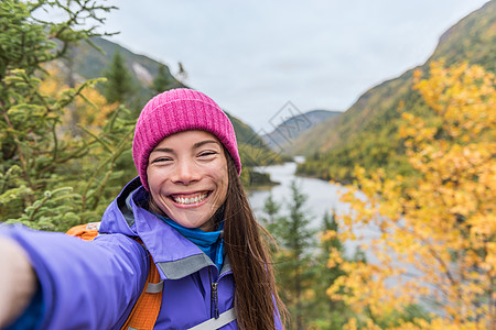 自拍亚洲女孩在秋季自然山区徒步旅行 快乐的徒步旅行者女人在秋天的山景户外拍摄智能手机照片手持电话在风景优美的观点 森林公园旅游生图片