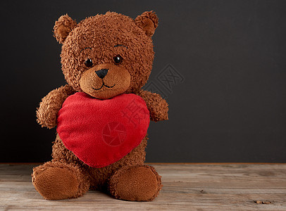 棕褐色可爱的泰迪熊 抱着红心 坐在一个臭嘴上图片