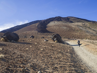 沙漠火山景观 孤独的徒步登山者攀爬在比科德三角山脉上 与黄 Teide的卵 滚动岩熔岩球相撞 其蓝天背景清晰图片