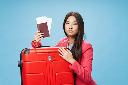 一名亚洲妇女带着手提箱外衣 出示护照和机票图片