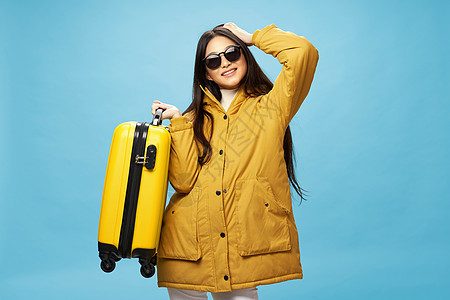 一个穿着温暖夹克的女孩 带着黄色手提箱 对着镜头微笑图片