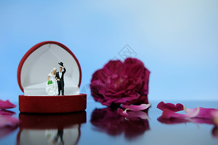 微型摄影户外婚礼概念 新娘和新郎站在红白玫瑰花堆上打开的戒指盒上方 玩具 浪漫的图片