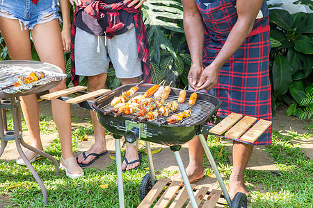 男人在烤烤烤肉烧烤炉上做饭 为家庭后院派对 野餐 火图片