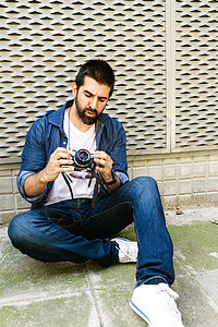 使用相机检查时坐在地上的胡子旅行者男子的身旁 专业的 1个图片