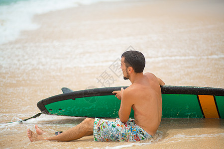 这家伙在冲浪后 正在沙沙热带海滩上休息 在夏季职业中健康活跃的生活方式 运动 自然图片