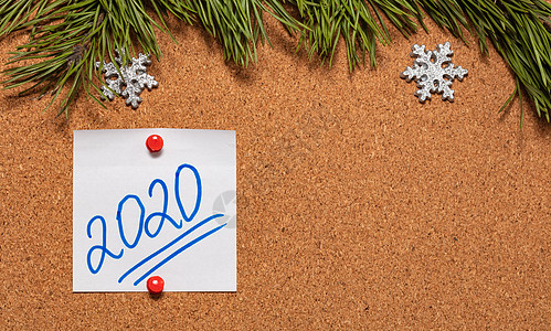 带有 2020 年手写体的白色便签贴在布告板上 布告板上装饰着松树枝和雪花 2020 年圣诞节 新年庆祝季节的概念 特写镜头 复背景图片