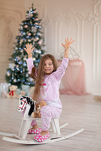 穿粉红色睡衣的漂亮小女孩 喜悦在木制摇石马上 这是圣诞圣诞礼物 玩具 庆典图片
