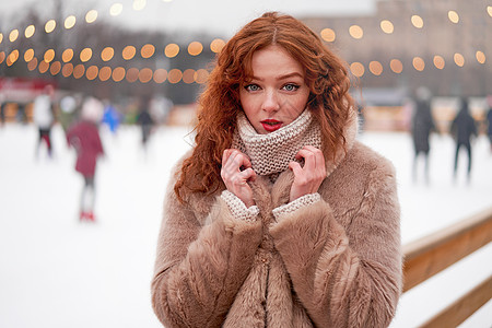 年轻漂亮的红发女孩在背景上有雀斑溜冰场 走在新年集市上的漂亮女人卷发肖像 冬天 假期图片