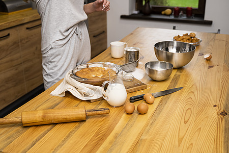 橡木桌上的美味苹果派 配料 穿着灰色睡衣的女人在阁楼风格的厨房里做美味的苹果派 牛奶 鸡蛋 糖和桌上的烤馅饼 家庭厨房 水果 手图片