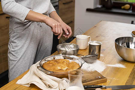 做糕点的女人橡木桌上的美味苹果派 配料 穿着灰色睡衣的女人在阁楼风格的厨房里做美味的苹果派 牛奶 鸡蛋 糖和桌上的烤馅饼 家庭厨房 面包师背景