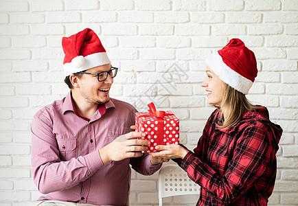 圣诞快乐的情侣在圣塔帽子庆祝节日 在白砖墙背景上庆祝图片