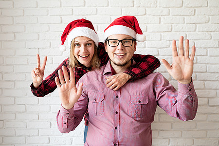 在白色砖墙背景的圣塔帽中 快乐的圣诞情侣 家 假期图片
