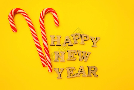 庆祝新年快乐 黄色背景新年帽上的木制字母 上面放着红色糖果 节日装饰或明信片概念 顶视图和平面 复制空间 闪光 假期图片