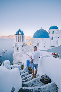 希腊圣托里尼岛日落 美丽的白洗的奥亚村 Oia 美丽 日落时有教堂和风车 青年男子在豪华度假 旅行 巡航图片