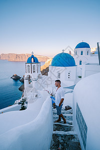 希腊圣托里尼岛日落 美丽的白洗的奥亚村 Oia 美丽 日落时有教堂和风车 青年男子在豪华度假 浪漫的 圆顶图片