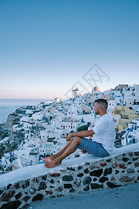 希腊圣托里尼岛日落 美丽的白洗的奥亚村 Oia 美丽 日落时有教堂和风车 青年男子在豪华度假 浪漫的 酒店图片