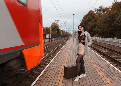 身着灰色大衣 手提箱站在火车站的年轻女孩 时尚 欧洲背景图片