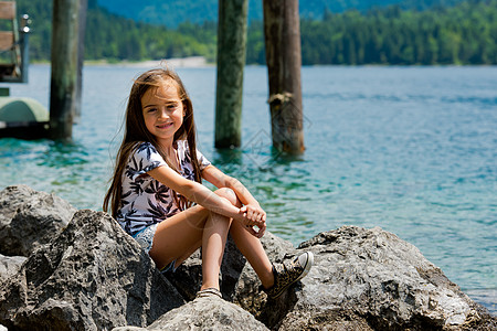 一位可爱的小姑娘坐在阿尔卑斯湖的岸边 在奥地利Plan See湖 女士 支撑图片