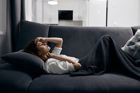 一个女人在舒适的房间里 睡在沙发上 裹着灰色毯子图片