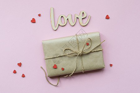 以棕色手工艺纸和领带绳包着的包裹展示在浅粉红色背景上 浪漫礼物 带有装饰红心 顶级视图 庆典 盒子图片
