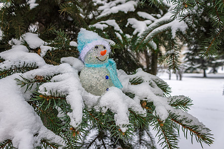 一只玩具雪人站在冬天的森林里 一片fir树上 被雪覆盖的刺状小枝上图片