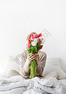 穿着睡衣坐在床上的妇女 当着面拿着郁金香花束在她面前图片
