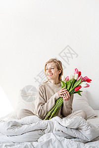 坐在床上的开心女人穿着睡衣 拿着郁金香花花束 浪漫的 爱图片