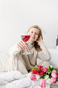 坐在床上的快乐女人穿着睡衣 拿着酒杯和郁金香花花束 花朵 房间图片