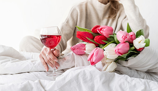 坐在床上的快乐女人穿着睡衣 拿着酒杯和郁金香花花束 卧室 葡萄酒图片