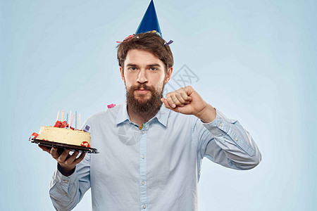 拿着一盘蛋糕和节日蜡烛蓝色背景帽公司聚会的男人 惊喜 乐趣图片