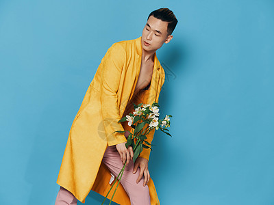 穿着黄色大衣和粉红色长裤的有吸引力的亚洲男子 手里拿着一束花束图片