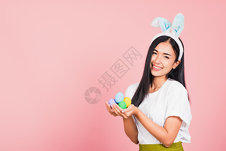 妇女笑着穿着兔子耳朵 手拿着彩色复活节鸡蛋礼物 奢华图片