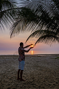 沙滩上日出时有棕榈树 泰国清川 在泰国海滩上看日落的男子 环境 热带图片