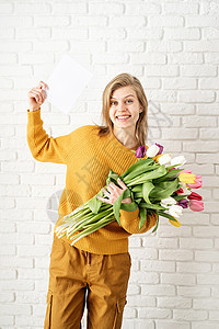 穿着黄色衣服的美丽美女 拿着郁金香花束和空白卡 漂亮的 惊喜图片