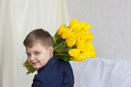 一个年轻 美丽的男孩 他肩膀上背着黄色的新郁金香 非常有害 3月8日国际妇女节春季和假日的概念 季节 舒适图片