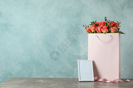 带粉红玫瑰花束和灰色桌上空框的礼品袋 以浅面为背景图片