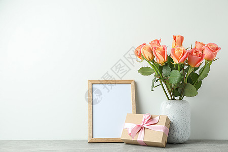 白色背景的灰色桌子上带玫瑰 礼物和空框的花瓶 文字空间图片