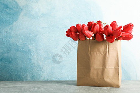 红色纸袋在蓝色背景 文字空间的桌上桌边有漂亮的红色红色郁金香纸袋 天 花束背景
