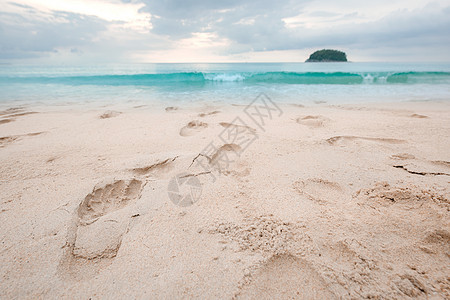 美丽的沙滩上的脚印 和日落时的松绿海水 海浪图片