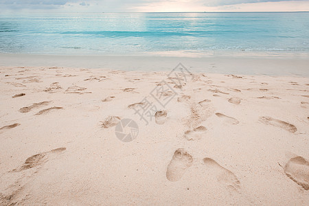 美丽的沙滩上的脚印 和日落时的松绿海水 海浪图片