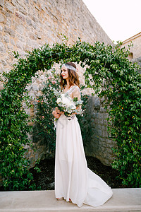 欧洲藤本月季花新娘站在古老的布德瓦镇 一个与野葡萄连在一起的优美的拱门上 手里握着一束花束背景