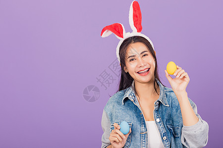 戴着兔子耳朵微笑的女人和戴尼姆人手握着丰富多彩的复活节鸡蛋礼物 庆典 奢华图片