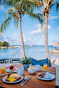 在海滩边的桌子上享用早餐 俯瞰大海 加勒比海 早餐桌上供应咖啡 橙汁 羊角面包和水果 蓝色的 玻璃图片