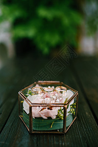 新郎新娘的结婚戒指和装饰玻璃盒上的订婚戒指 里面有一朵粉色的花图片