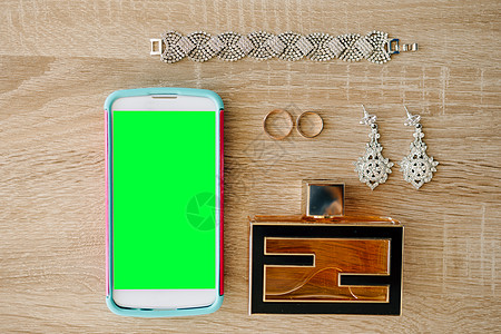 耳环 戒指 手镯和香水旁边的木制桌子上有带空白屏幕的智能手机图片