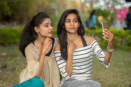 两位美丽的女性朋友在户外用智能手机拍自拍 快乐的 冒充图片
