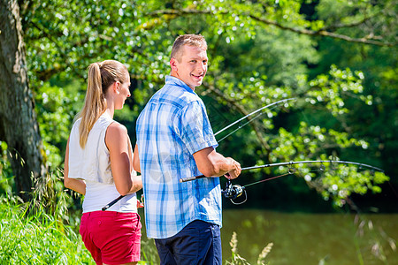 年轻夫妇在河岸捕鱼或钓鱼 或站立在河岸上 运动 池塘图片